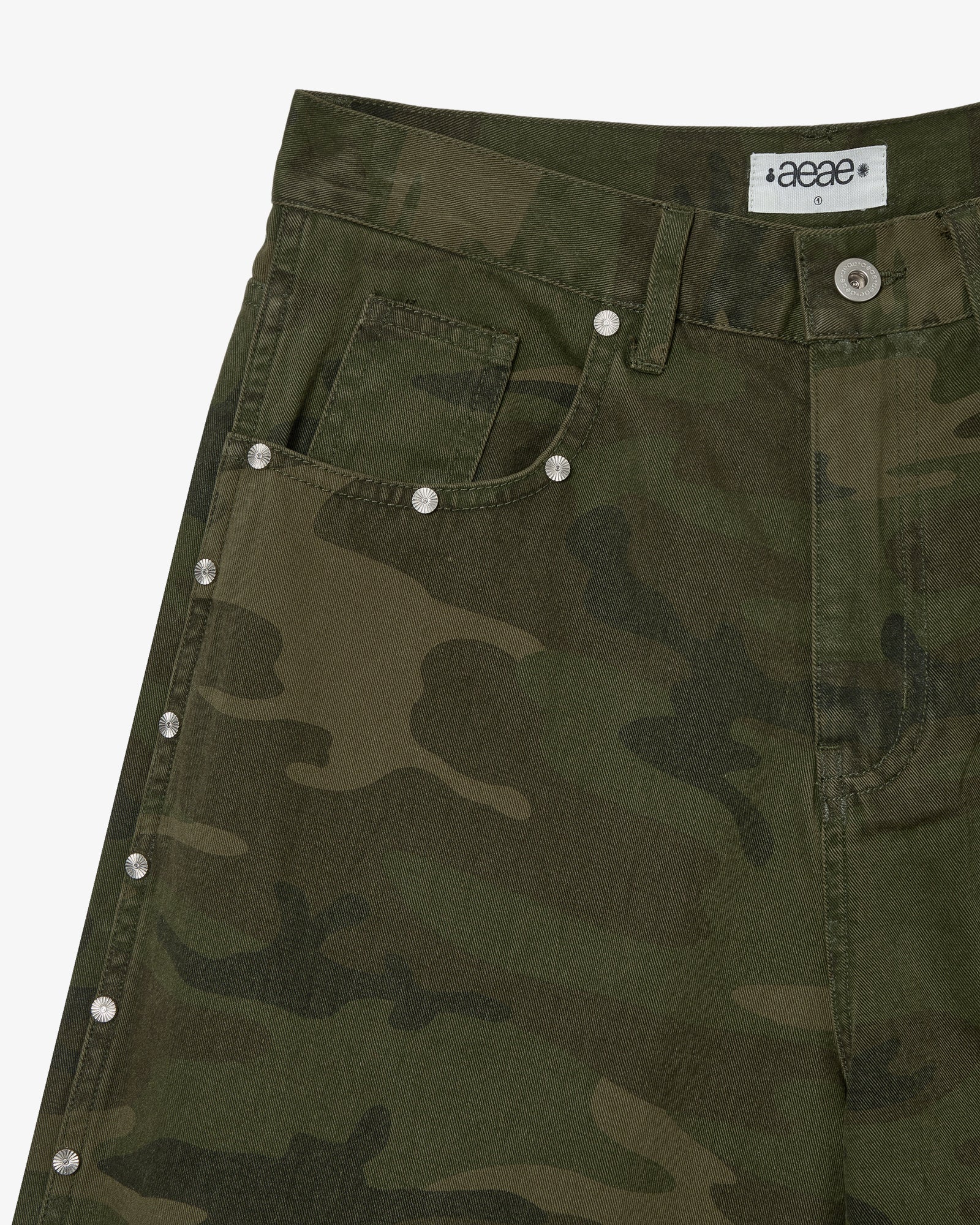 The front side pocket of a pair of shorts in a camouflage print with silver studs on the side seams from Korean brand aeae, for sale at Shim House