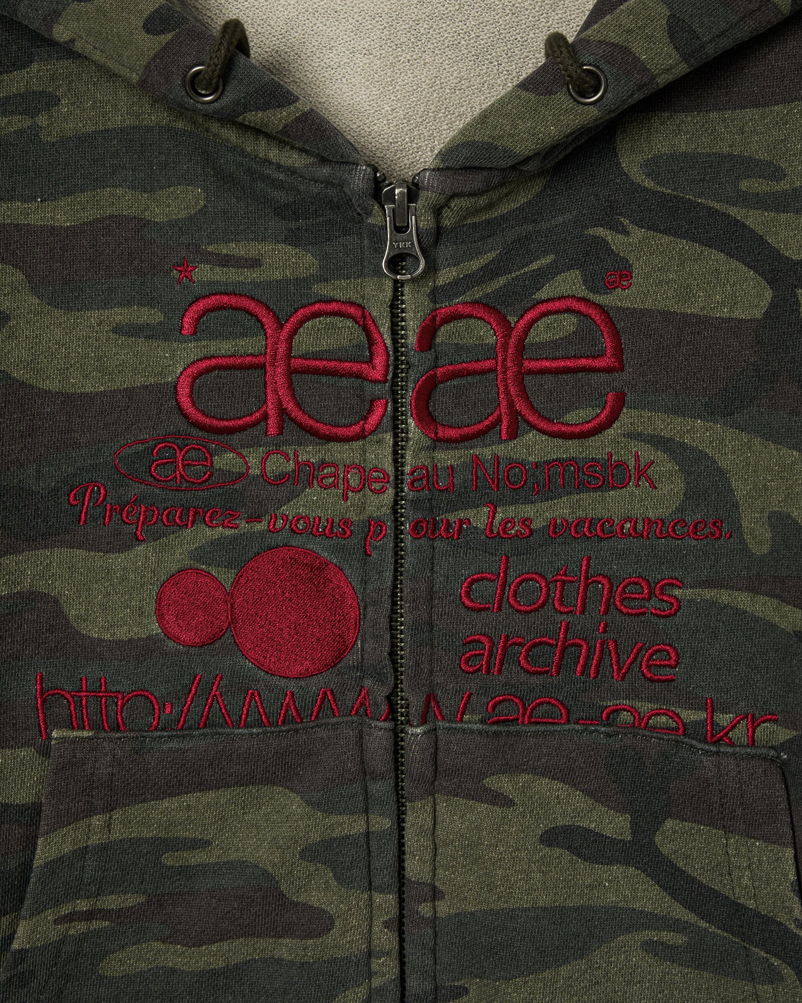 A close up of a cropped zip through hoodie that has a camouflage print and red embroidery from Korean brand aeae, for sale at Shim House