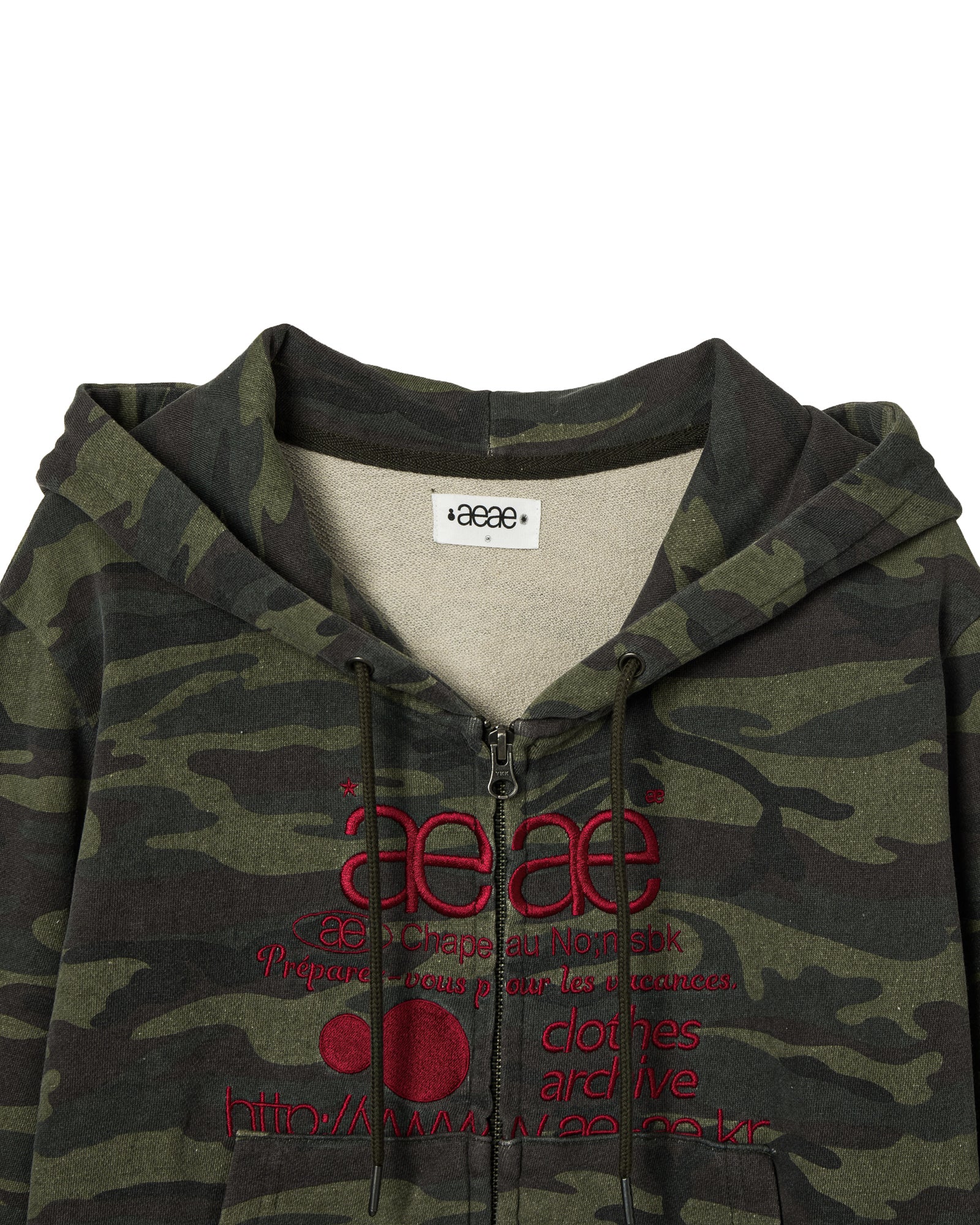 A close up of a cropped zip through hoodie that has a camouflage print and red embroidery from Korean brand aeae, for sale at Shim House